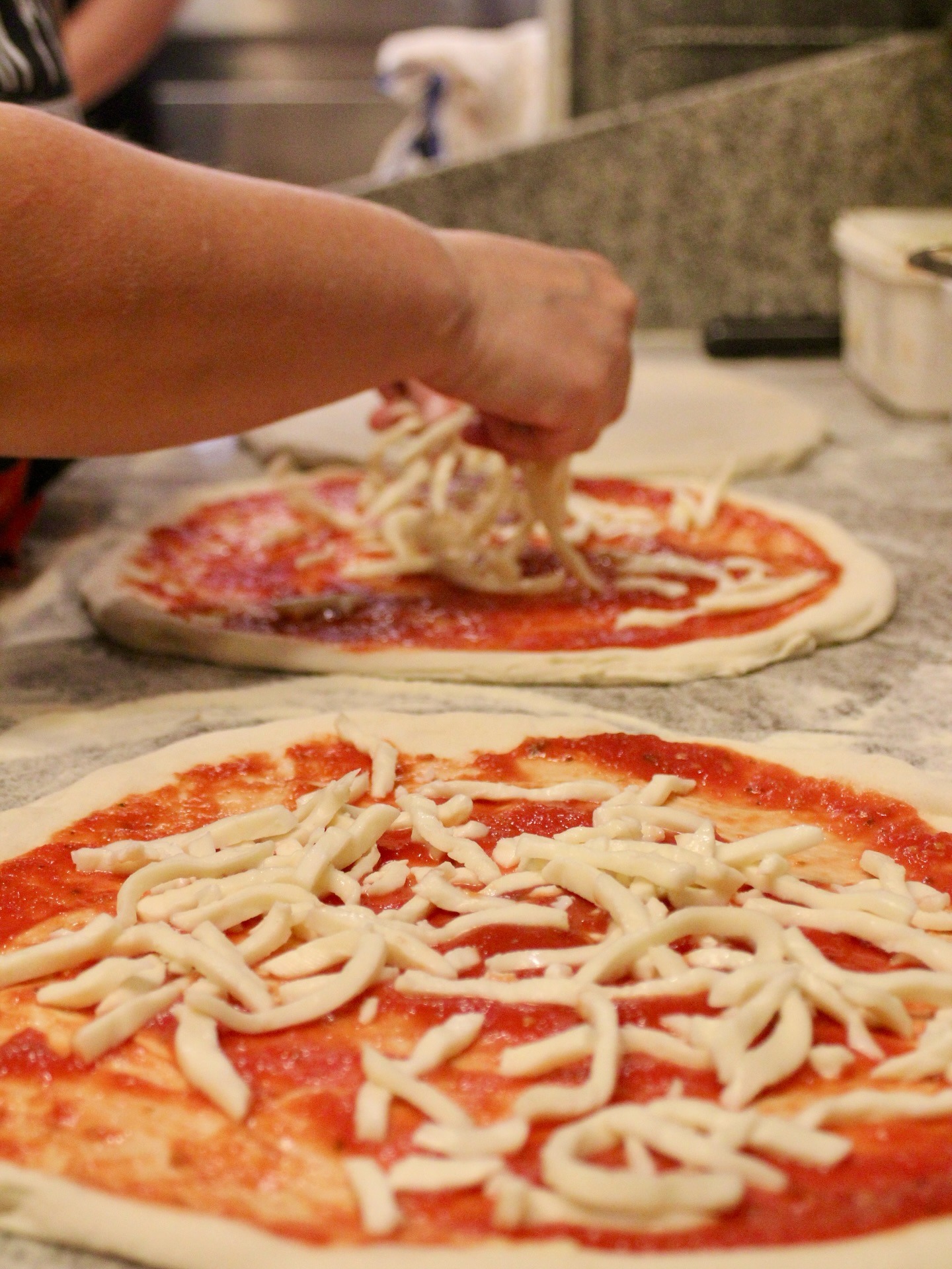Chef hand-layering fresh mozzarella onto pizza dough
