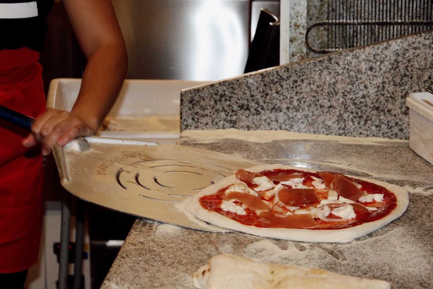 Pizza sliding into the stone oven on a peel