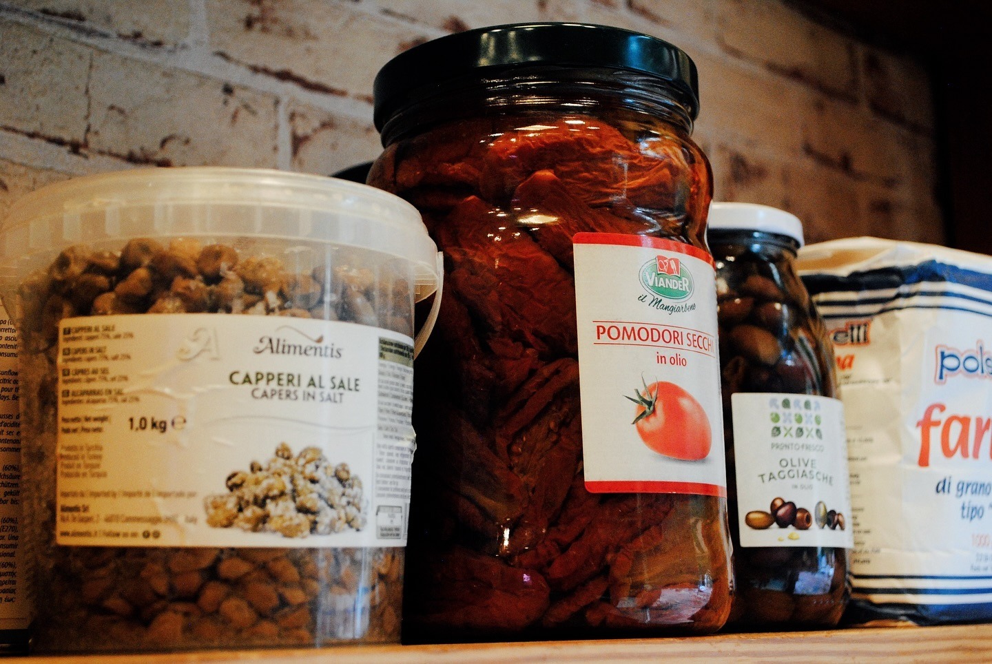 Shelf of imported Italian ingredients: capers, sun-dried tomatoes, olives, flour
